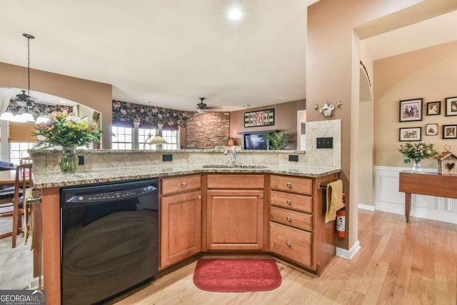 kitchen with brown cabinetry, dishwasher, wainscoting, light stone countertops, and a sink