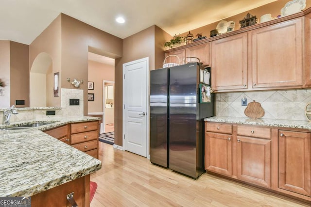 kitchen with light wood finished floors, tasteful backsplash, light stone counters, freestanding refrigerator, and a sink