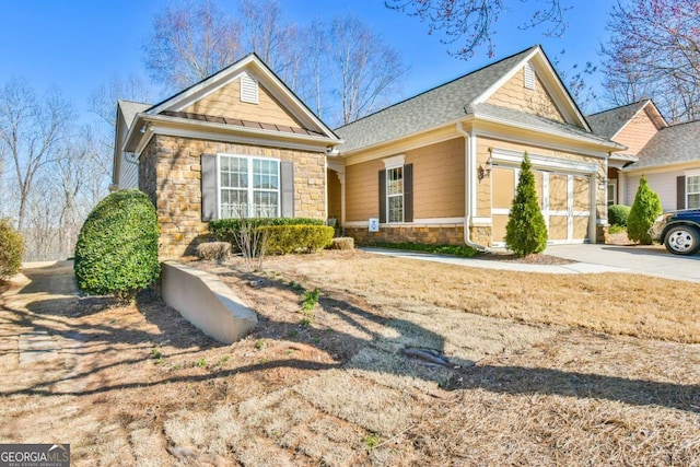 view of front of property with stone siding, roof with shingles, and driveway