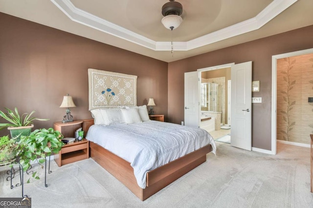 bedroom with a tray ceiling, light colored carpet, ornamental molding, connected bathroom, and baseboards