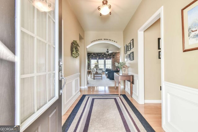 entrance foyer featuring light wood-style floors, arched walkways, a wainscoted wall, and a decorative wall