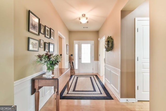 doorway featuring a wainscoted wall, wood finished floors, visible vents, and a decorative wall