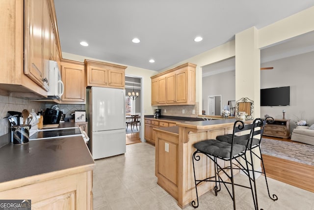 kitchen with white appliances, light brown cabinets, open floor plan, a peninsula, and a kitchen bar