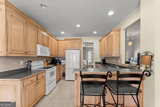 kitchen with light brown cabinets, recessed lighting, white appliances, dark countertops, and a kitchen bar