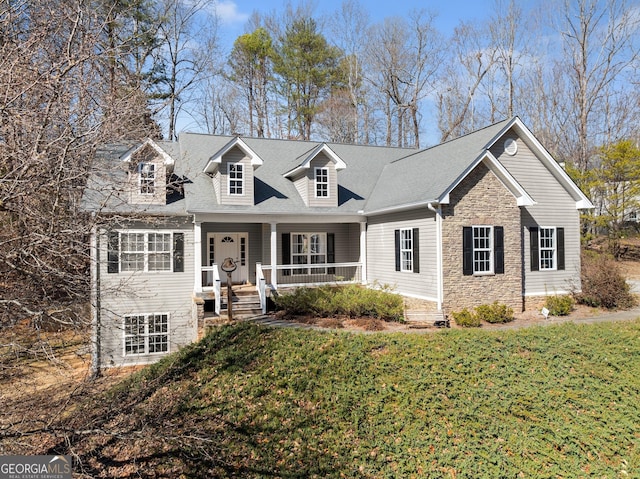 cape cod home with covered porch, stone siding, roof with shingles, and a front yard