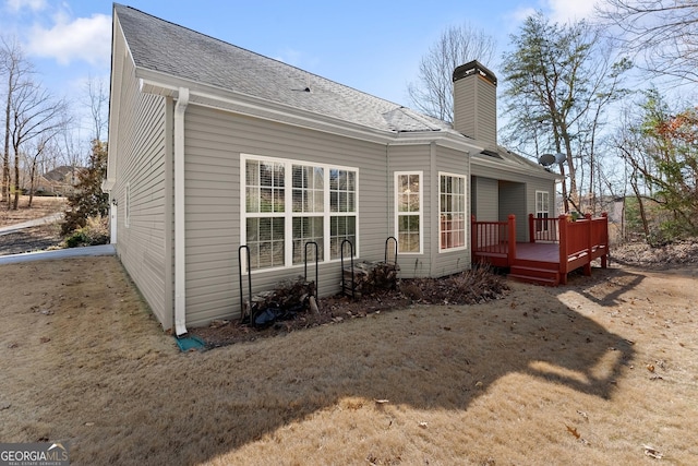 rear view of property with roof with shingles, a chimney, and a wooden deck