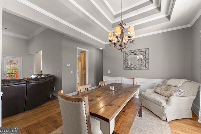 dining room featuring a chandelier, a wainscoted wall, wood finished floors, a raised ceiling, and crown molding