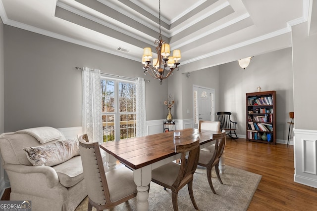 dining space with a chandelier, a raised ceiling, wainscoting, and wood finished floors