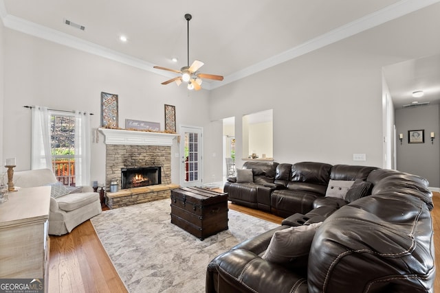 living area with visible vents, a high ceiling, ornamental molding, a stone fireplace, and wood finished floors