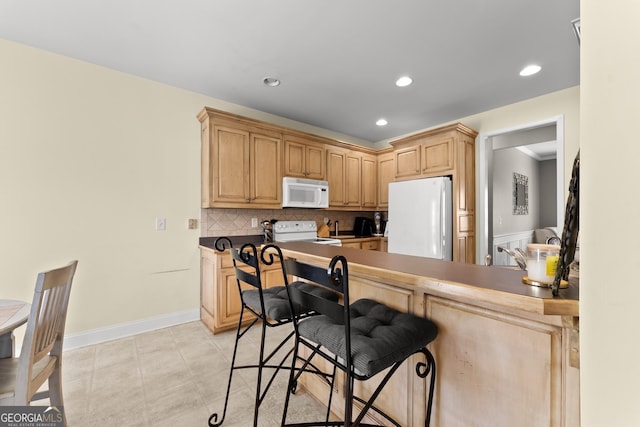 kitchen featuring light brown cabinets, recessed lighting, white appliances, baseboards, and backsplash