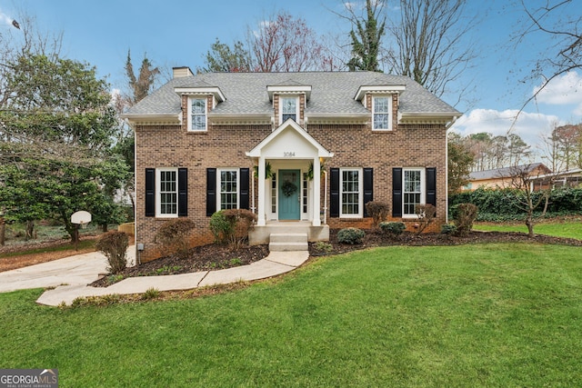 view of front facade featuring a front lawn, brick siding, roof with shingles, and a chimney