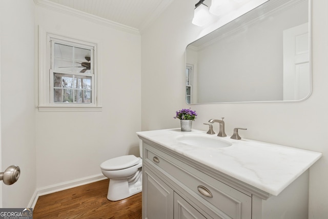 half bathroom with vanity, wood finished floors, baseboards, crown molding, and toilet