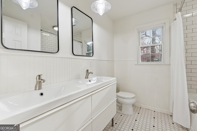 bathroom with a sink, toilet, double vanity, and wainscoting