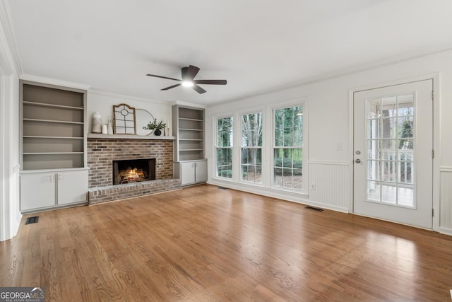 unfurnished living room featuring visible vents, a healthy amount of sunlight, a ceiling fan, and built in features