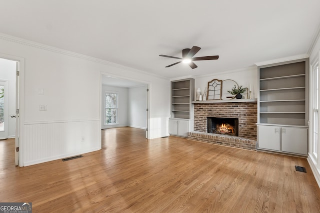 unfurnished living room featuring visible vents, built in shelves, light wood-type flooring, and ceiling fan