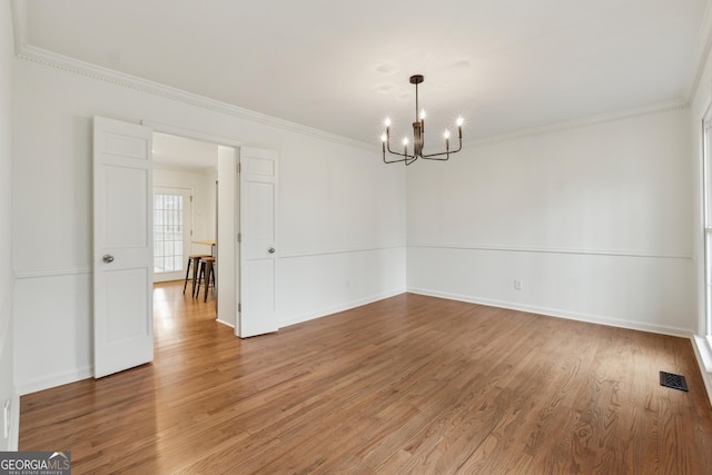 spare room featuring a chandelier, baseboards, light wood-style floors, and ornamental molding