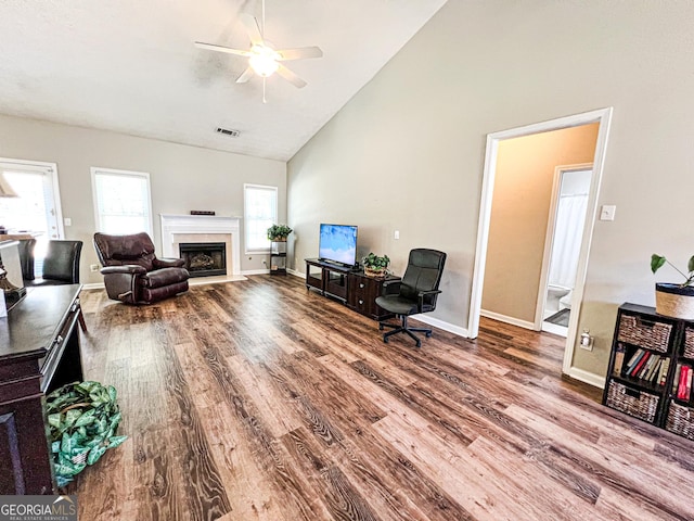 living area featuring a premium fireplace, visible vents, high vaulted ceiling, and wood finished floors