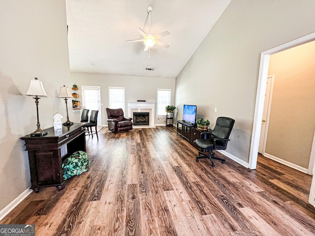 sitting room with a fireplace with flush hearth, wood finished floors, baseboards, and high vaulted ceiling