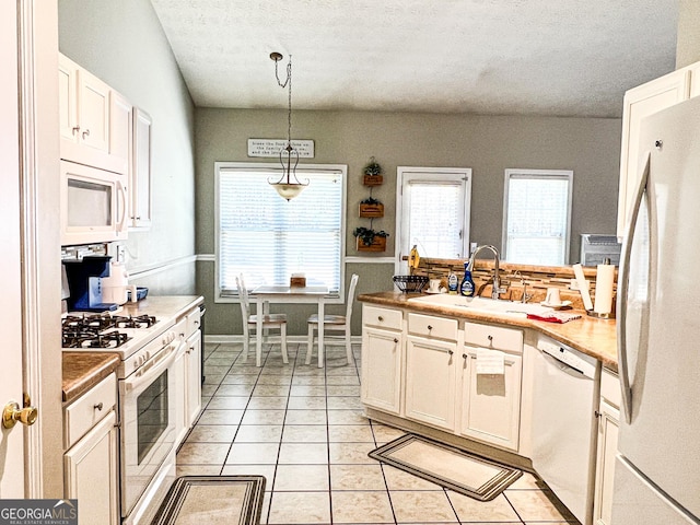 kitchen with pendant lighting, light tile patterned flooring, white appliances, white cabinetry, and a sink