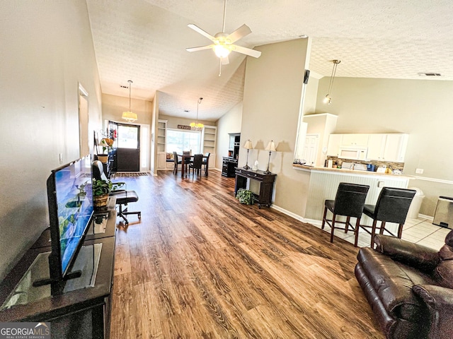 living area featuring baseboards, high vaulted ceiling, wood finished floors, a textured ceiling, and a ceiling fan