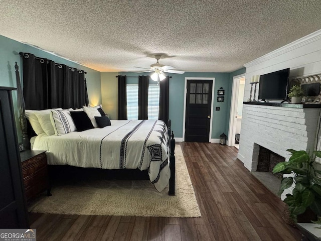 bedroom with dark wood-type flooring, a ceiling fan, a brick fireplace, a textured ceiling, and baseboards