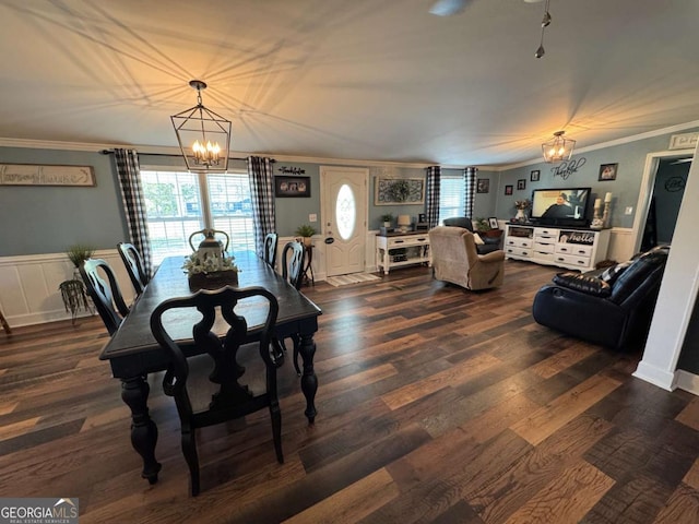 dining area featuring wainscoting, ornamental molding, dark wood-type flooring, an inviting chandelier, and a decorative wall