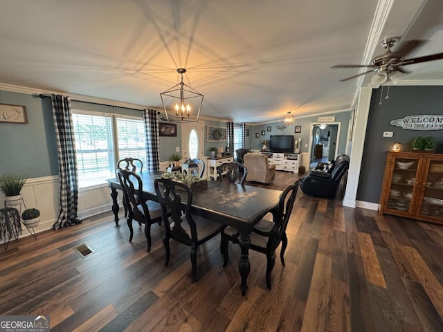 dining area with dark wood-style floors, ceiling fan, ornamental molding, and a wainscoted wall