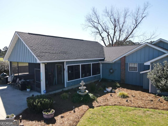 view of front facade with a sunroom, a shingled roof, a patio area, and board and batten siding