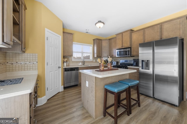 kitchen featuring a breakfast bar area, wood finished floors, a center island, appliances with stainless steel finishes, and decorative backsplash