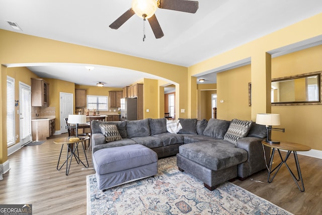 living room featuring arched walkways, wood finished floors, visible vents, and baseboards