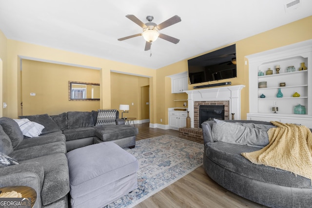 living room featuring a ceiling fan, visible vents, a fireplace, and wood finished floors