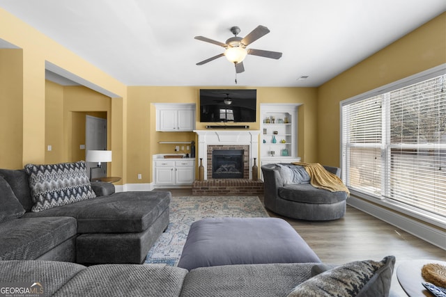living room featuring wood finished floors, a brick fireplace, baseboards, and ceiling fan