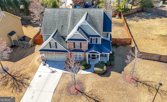 view of front facade with a garage, a shingled roof, concrete driveway, fence, and brick siding