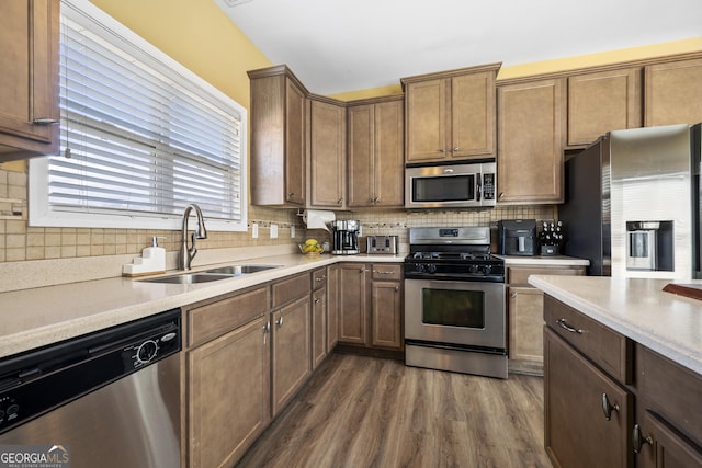 kitchen with tasteful backsplash, dark wood-style floors, stainless steel appliances, light countertops, and a sink