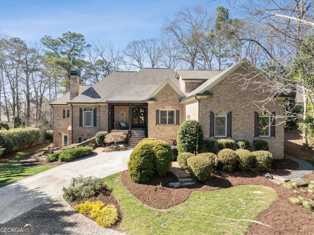 view of front of property featuring driveway, a chimney, and brick siding