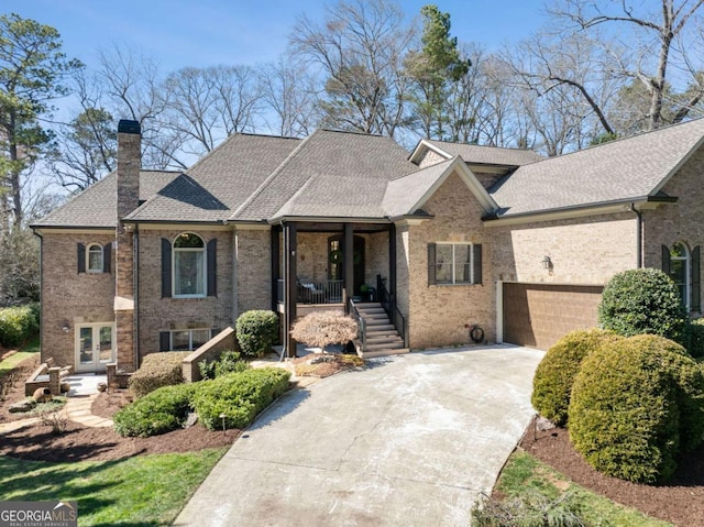 view of front of house with french doors, roof with shingles, brick siding, a chimney, and driveway