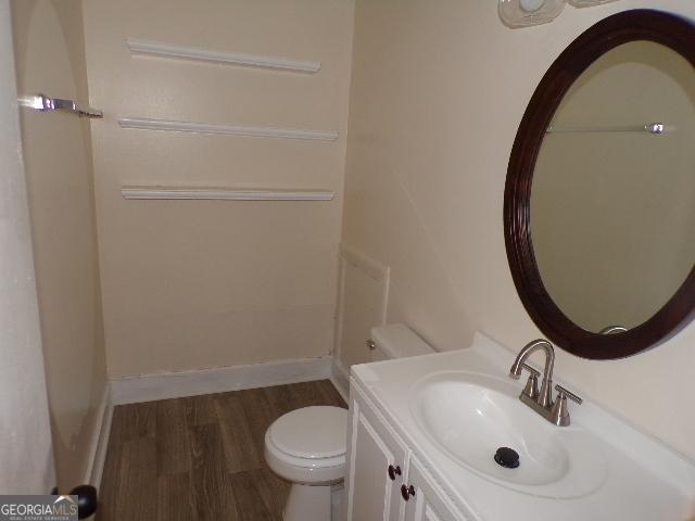 bathroom with wood finished floors, vanity, toilet, and baseboards