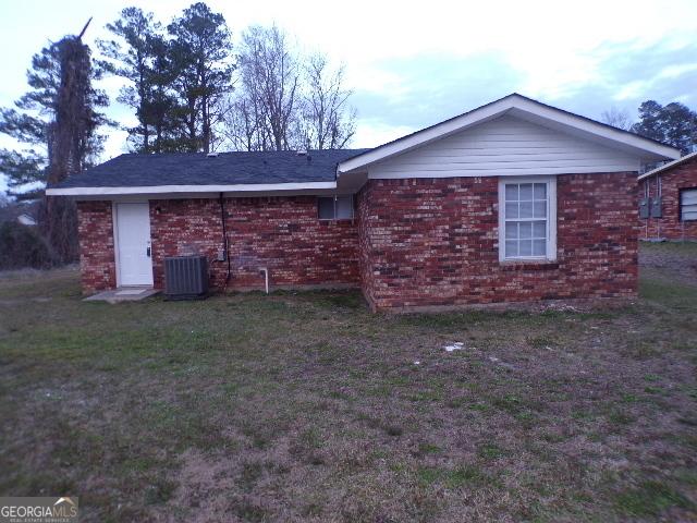 view of home's exterior with central AC, brick siding, and a lawn