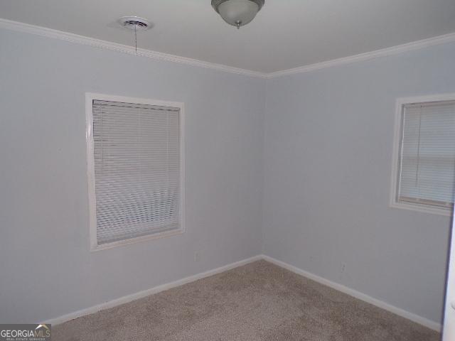 carpeted empty room featuring baseboards, visible vents, and ornamental molding