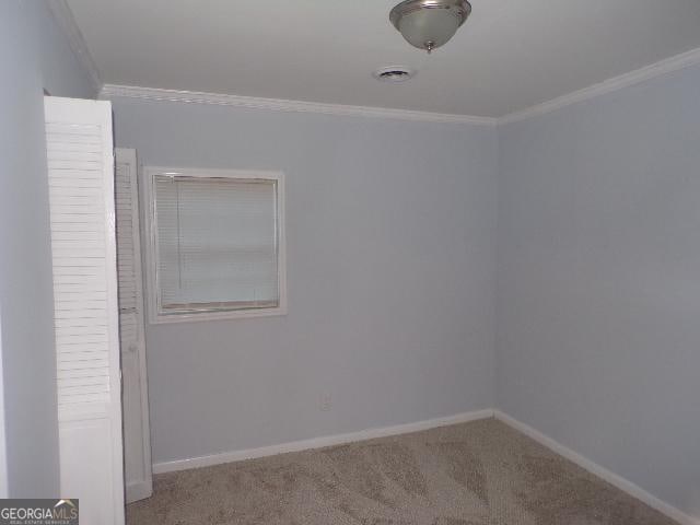 carpeted empty room with visible vents, crown molding, and baseboards