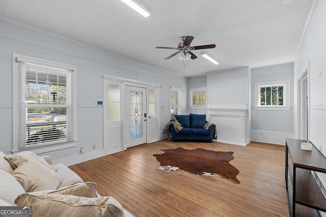 living area with baseboards, crown molding, hardwood / wood-style flooring, and a ceiling fan