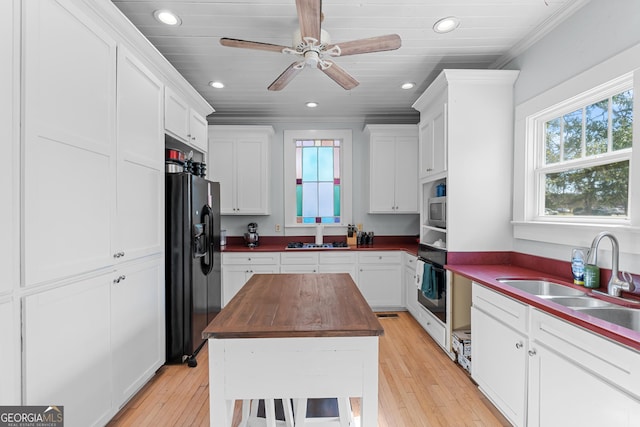 kitchen with a wealth of natural light, butcher block counters, white cabinets, a sink, and black appliances