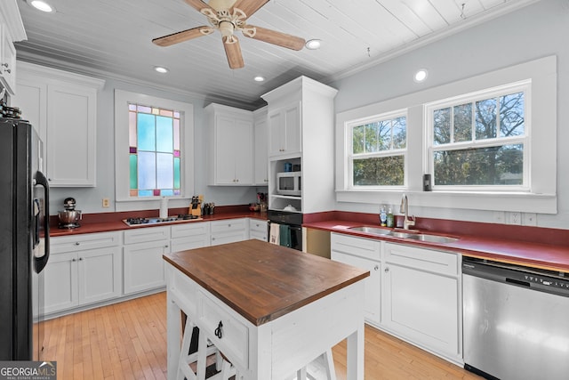 kitchen with appliances with stainless steel finishes, butcher block countertops, a sink, and white cabinetry