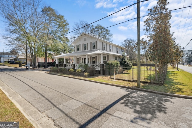 farmhouse with a porch, a fenced front yard, and a front lawn