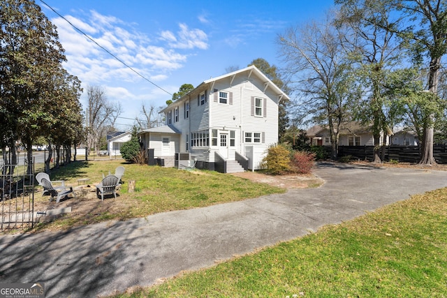 view of front facade with entry steps, an outdoor fire pit, fence, and a front lawn