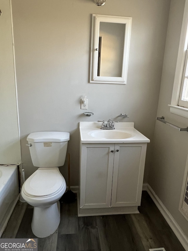 bathroom with toilet, a bathing tub, wood finished floors, vanity, and baseboards