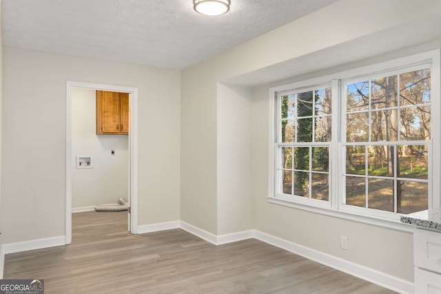 spare room featuring light wood-type flooring, baseboards, and a textured ceiling