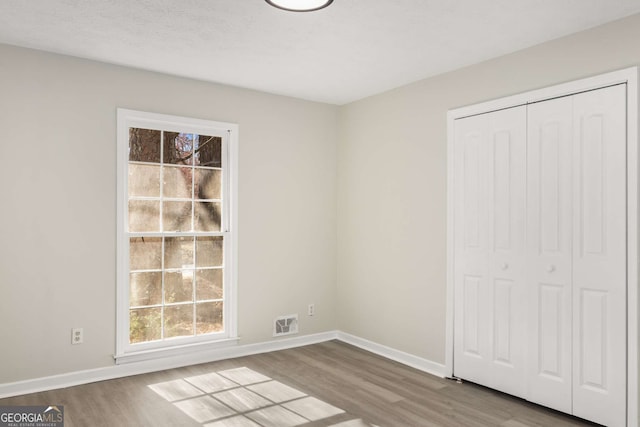 unfurnished bedroom featuring visible vents, baseboards, a closet, and wood finished floors