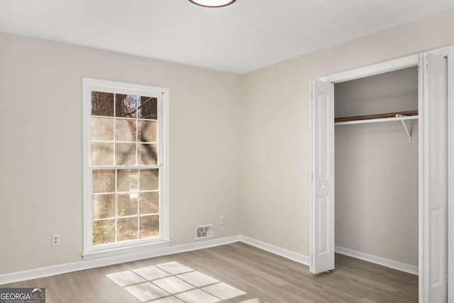 unfurnished bedroom with a closet, wood finished floors, visible vents, and baseboards