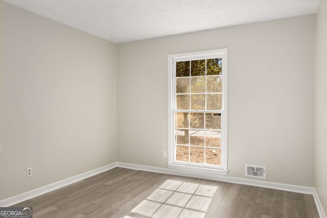 unfurnished room with a wealth of natural light, wood finished floors, visible vents, and baseboards